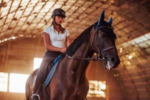 majestuosa imagen de silueta de caballo con jinete sobre fondo de puesta de sol. la chica jockey en la parte trasera de un semental monta en un hangar en una granja foto