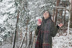 Finally some snowfall. Girl in warm clothes with cup of coffee have a walk in the winter forest photo
