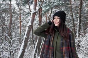 Positivity in cold season of the year. Cheerful young girl in warm clothes have a walk in the winter forest at daytime photo