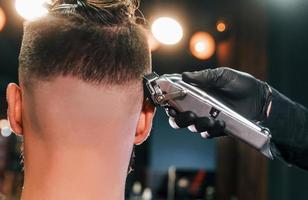 Close up view of young bearded man that sitting and getting haircut in barber shop photo