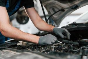 Under the hood. Man in work uniform repairs white automobile indoors. Conception of automobile service photo