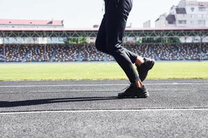 Close up view of legs of runner in black pants and shoes that is outdoors on the track photo