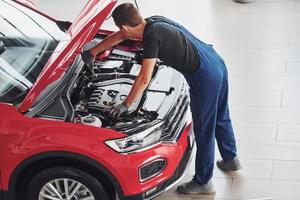 Top view of male worker in uniform that repairs red automobile photo