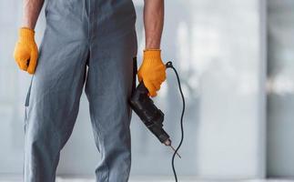 Close up view of man in grey uniform with drill in hand indoors in modern big office at daytime photo