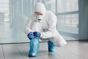 Male doctor scientist in lab coat, defensive eyewear and mask wearing protective material on legs photo