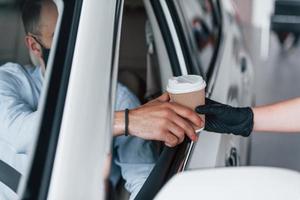 Buying fresh drink. Young handsome man in formal clothes and protective mask sitting in brand new automobile photo