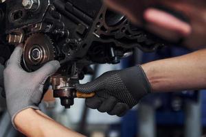 Professional repairman in black protective mask works with broken automobile engine photo