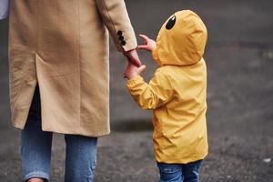 Kid in yellow waterproof cloak holding mother's hand and have a walk outdoors photo
