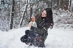 Dog want to go while girl petting him. Smiling brunette having fun while walking with her pet in the winter park photo