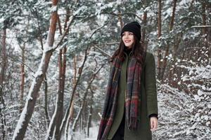 de pie en medio del bosque. una joven alegre con ropa de abrigo da un paseo por el bosque de invierno durante el día