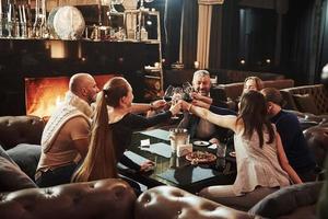 golpeando vasos. los amigos de la familia tienen una agradable velada cerca de la chimenea en un restaurante moderno de lujo foto