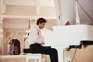 joven músico profesional con ropa oficial toca el piano blanco foto