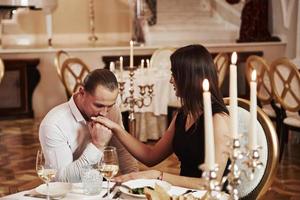 Takes woman's hand to kiss it. Beautiful couple have romantic dinner in luxury restaurant at evening time photo
