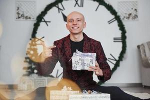 Man with big clock behind him sitting with New year gift boxes in holiday clothings photo