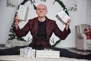 Look what I have. Man with big clock behind him sitting with New year gift boxes in holiday clothings photo