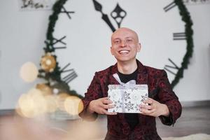 simplemente sonriendo y divirtiéndome. hombre con un gran reloj detrás de él sentado con cajas de regalo de año nuevo en ropa de vacaciones foto