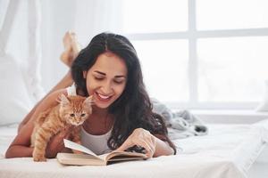 Time to read. Attractive blonde resting on the white bed with her cute kitten photo