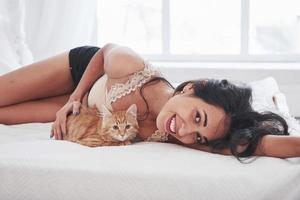 Lying together. Attractive blonde resting on the white bed with her cute kitten photo