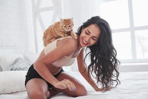 Playful kitten is on the shoulders. Girl have weekend sitting on the bed. Brunette resting on the couch photo