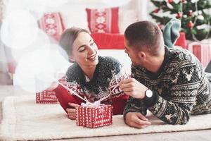 Hope it's what I think. Lovely young couple lying on the floor of living room at new year time with gift boxes photo