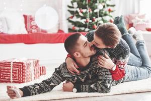 Making photo of cute kiss. Lovely young couple lying on the floor of living room at new year time with gift boxes