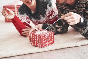 Process of opening the present. Lovely young couple lying on the floor of living room at new year time with gift boxes photo