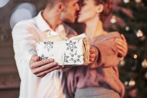 besándose mientras sostiene la caja de regalo. gente linda. linda pareja celebrando el año nuevo en la habitación decorada de año nuevo foto