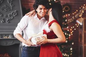 Thankful woman hugs her man. Beautiful couple celebrating New year in the decorated room with Christmas tree behind photo