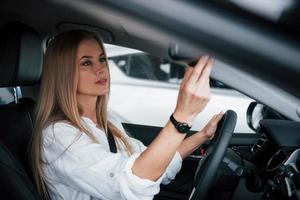 mujer adulta seria. hermosa chica rubia sentada en el auto nuevo con interior negro moderno foto