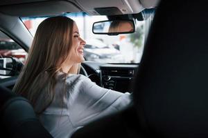 Me enamoré de este vehículo. hermosa chica rubia sentada en el auto nuevo con interior negro moderno foto