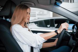 manejemos. hermosa chica rubia sentada en el auto nuevo con interior negro moderno foto