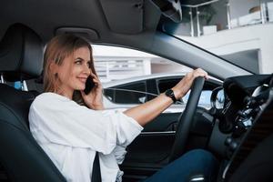 estoy en camino. hermosa chica rubia sentada en el auto nuevo con interior negro moderno foto