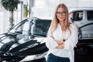 How can I help you. Young manager in the auto shop stands against perfectly polished black car