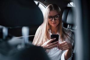 Wireless technologies. Smart businesswoman sits at backseat of the luxury car with black interior photo