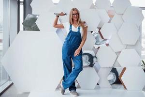 Silver colored wrench. Girl in blue uniform stands against abstract wall with white pieces of surface in the shape of hexagon in the auto saloon photo