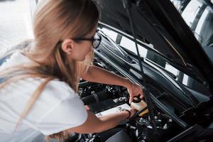 Oil replacement. On the lovely job. Car addicted woman repairs black automobile indoors photo