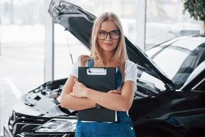 New customer is coming. Manager with notepad, in the white shirt and blue uniform stands against automobile with hood up photo