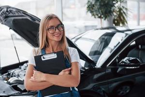 With natural lighting. Manager with notepad, in the white shirt and blue uniform stands against automobile with hood up photo