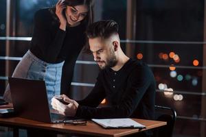 Girl is smiling. Team of young business people works on their project at night time in the office photo