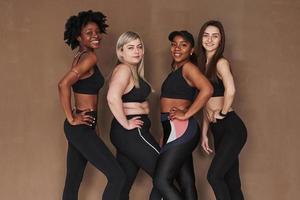 With sides turned to the camera. Group of multi ethnic women standing in the studio against brown background photo