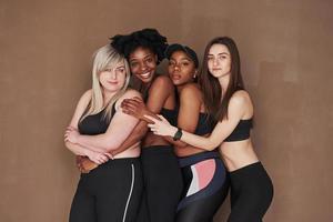 cercanía entre diferentes personas. grupo de mujeres multiétnicas de pie en el estudio con fondo marrón foto