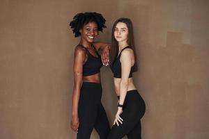 Standing together. Two multi ethnic female friends is in the studio with brown background photo