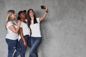 saluda a mis amigos. grupo de mujeres multiétnicas de pie en el estudio con fondo gris foto