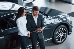 Making some notes. Female customer and modern stylish bearded businessman in the automobile saloon photo