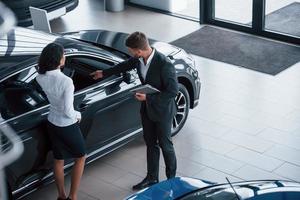 Showing features of the car. Female customer and modern stylish bearded businessman in the automobile saloon photo