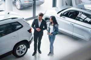 In jeans and white shirt. Female customer and modern stylish bearded businessman in the automobile saloon photo