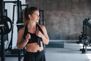 Black colored jumping rope. Photo of gorgeous blonde woman in the gym at her weekend time