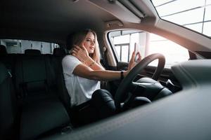 Beautiful and charmful. Girl in modern car in the salon. At daytime indoors. Buying new vehicle photo