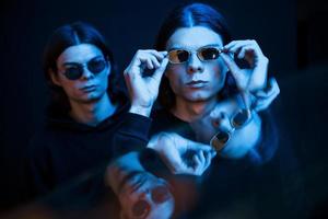 Wearing sunglasses. Portrait of twin brothers. Studio shot in dark studio with neon light photo