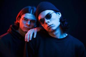 Leaning on the brother. Portrait of twins. Studio shot in dark studio with neon light photo